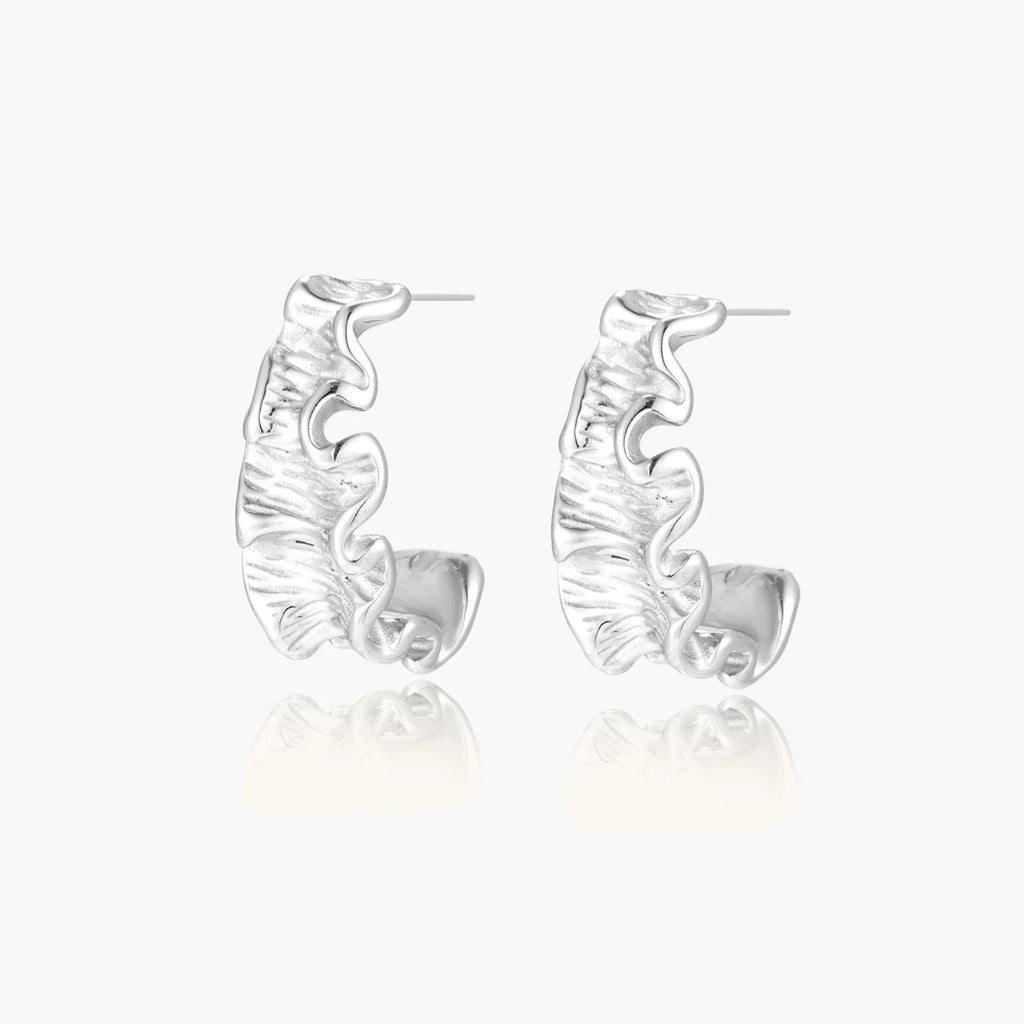 White gold plated sculptural hoop earrings with organic wavy edges and reflective metallic finish on cream background