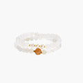 Three layered white beaded bracelets with carved orange agate lotus centerpiece and freshwater pearls on cream background.