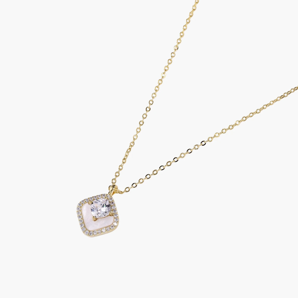 Gold quatrefoil pendant with crystal center on iridescent mother-of-pearl base, adjustable gold chain on cream background