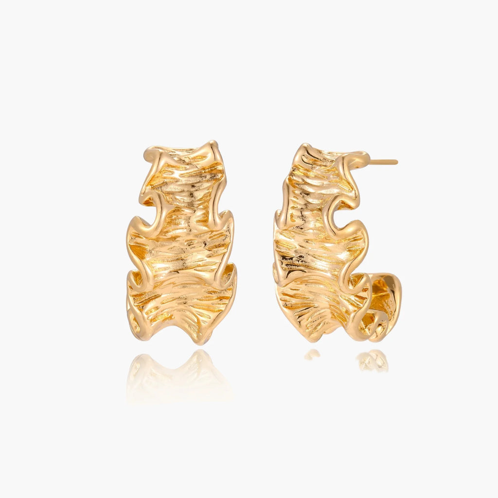 Pair of gold huggie hoops with sculpted wave texture and dimensional ripples on neutral background.