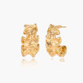 Pair of gold huggie hoops with sculpted wave texture and dimensional ripples on neutral background.