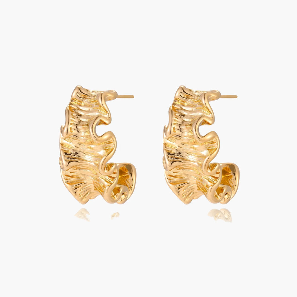 Pair of gold huggie hoops with sculpted wave texture and dimensional ripples on neutral background.