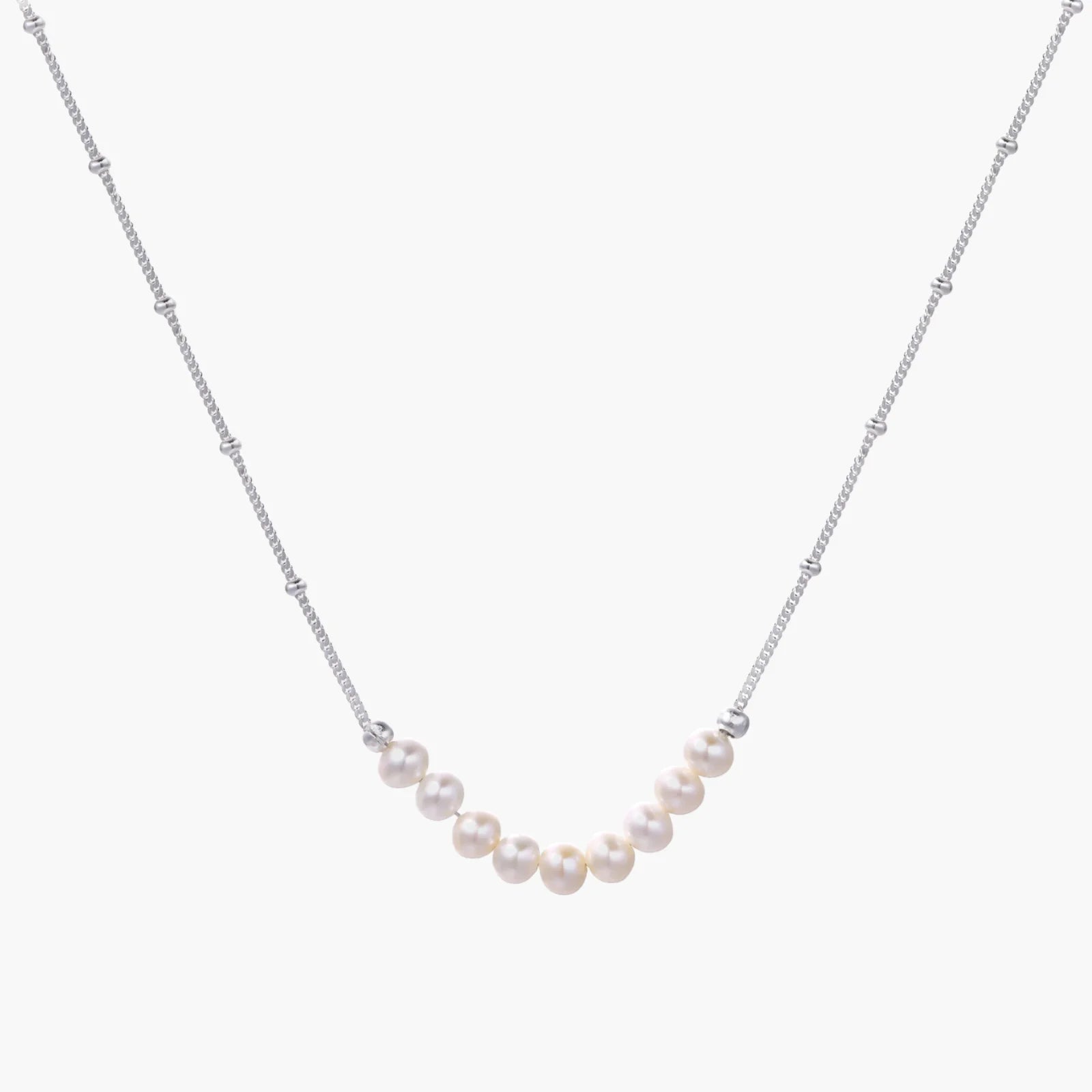 Delicate sterling silver chain necklace with small freshwater pearls arranged in a curved smile arc on cream background.