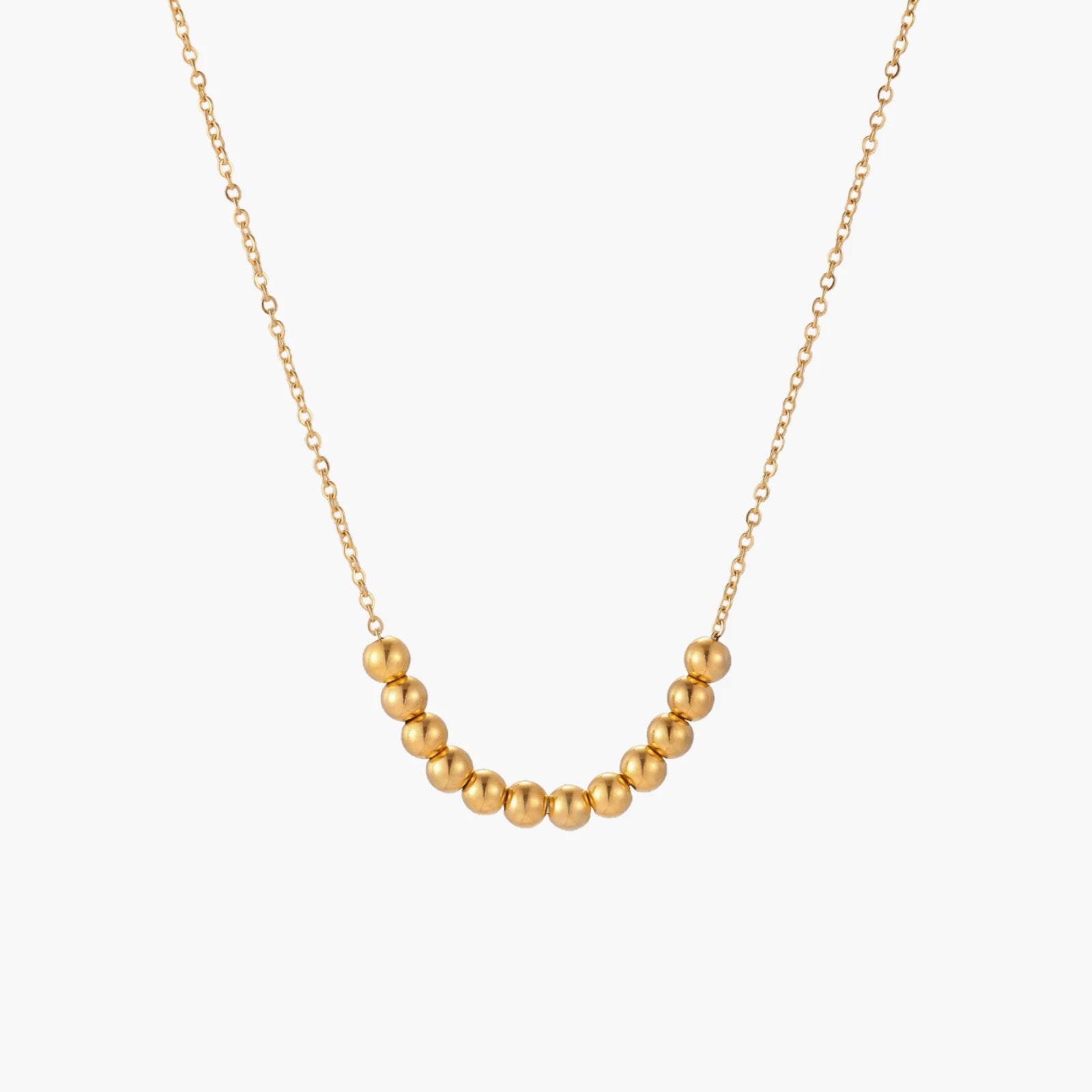 Delicate gold-plated necklace with graduated spherical beads forming gentle smile curve on beige background