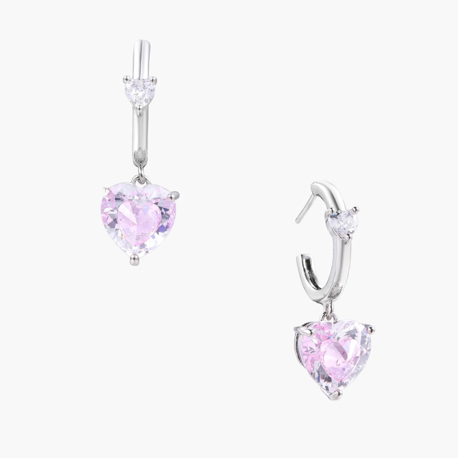 Silver huggie hoops with pink heart-cut zirconia pendants on white background, eco-friendly white gold plated brass