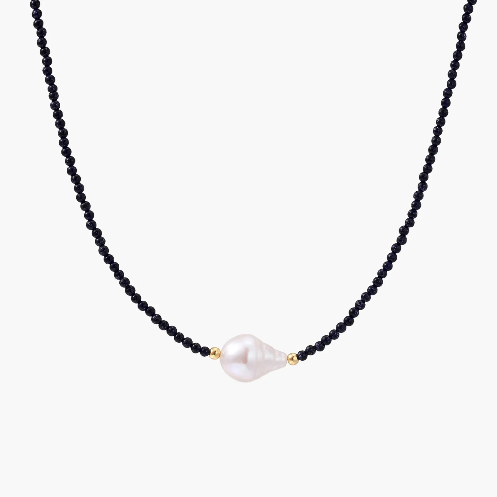 Delicate necklace with black blue sandstone beads and baroque pearl center on white background with gold accents.