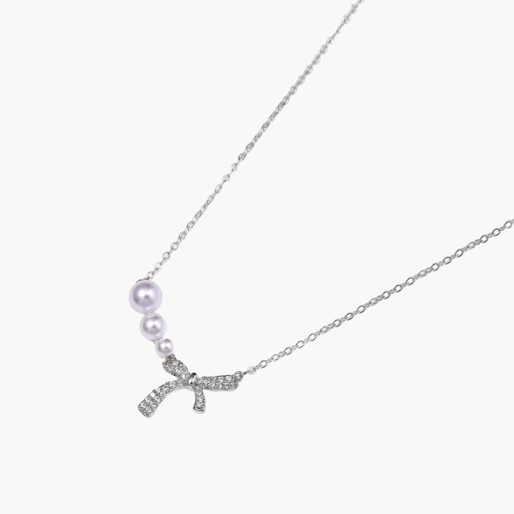 Delicate white gold plated necklace with graduated freshwater pearls and crystal-studded bow pendant on ivory background