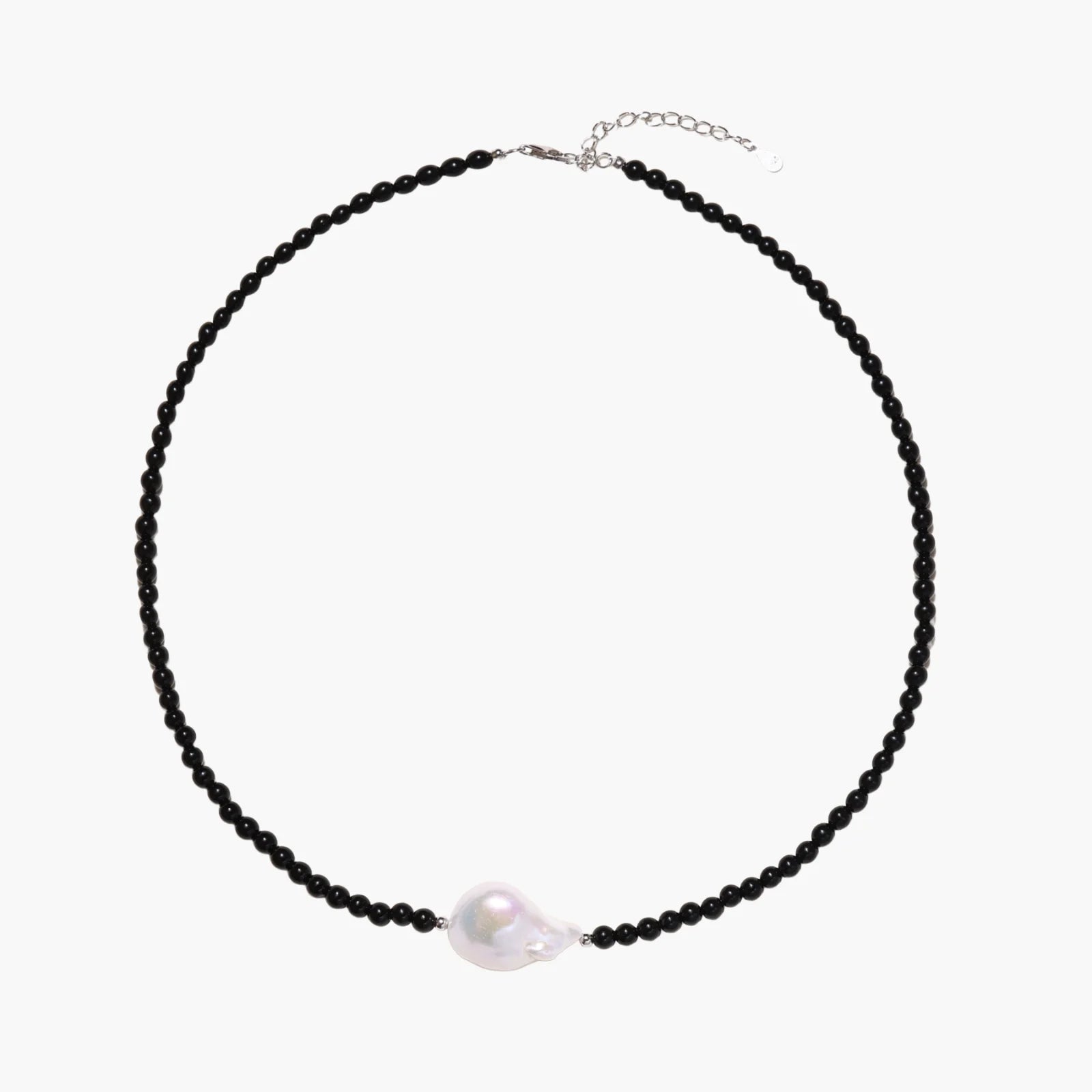 Beaded black agate necklace with iridescent baroque freshwater pearl centerpiece on cream background.