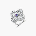 Flower-shaped sterling silver ring with brilliant round moissanite center stone and crystal petals on neutral background