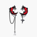 Gothic asymmetrical earrings with red crescent moons, black dripping stars, chains and crystal drop on white background.