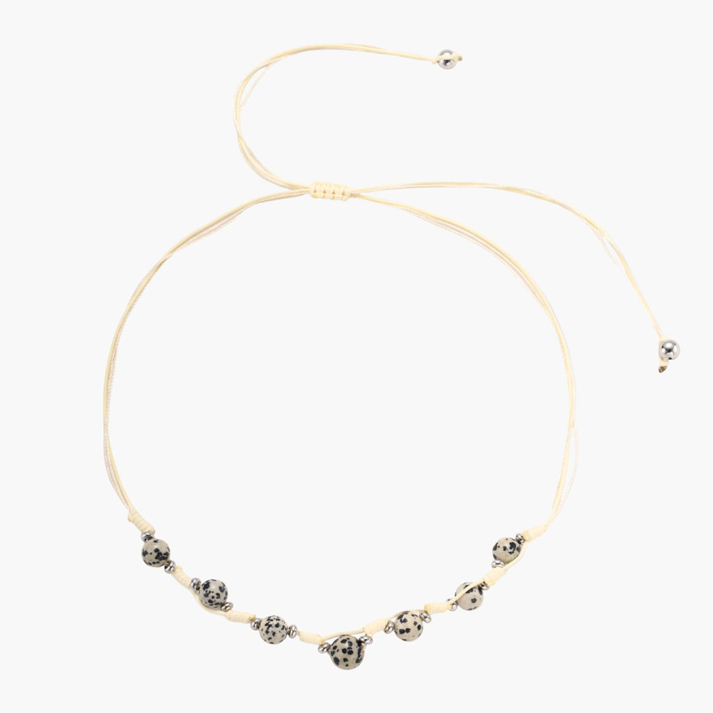 Adjustable cream cord necklace with white spotted stone beads featuring black speckles on neutral background