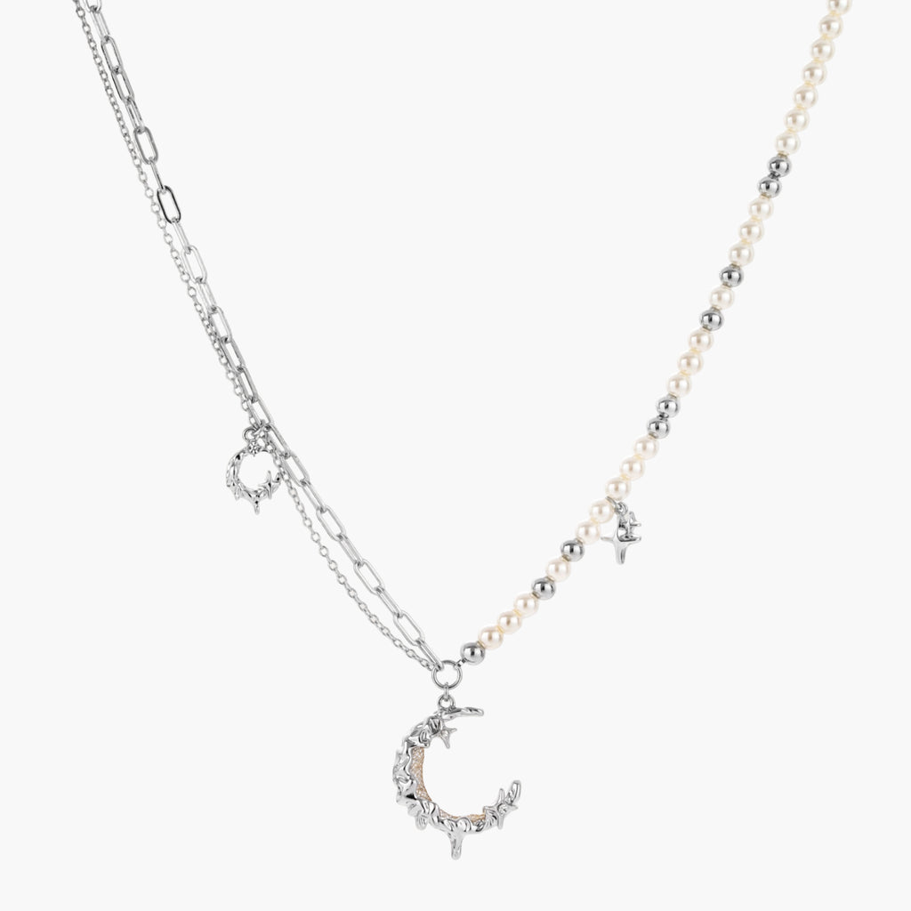 Silver-toned crescent moon pendant with star accents on pearl and chain necklace against white background.