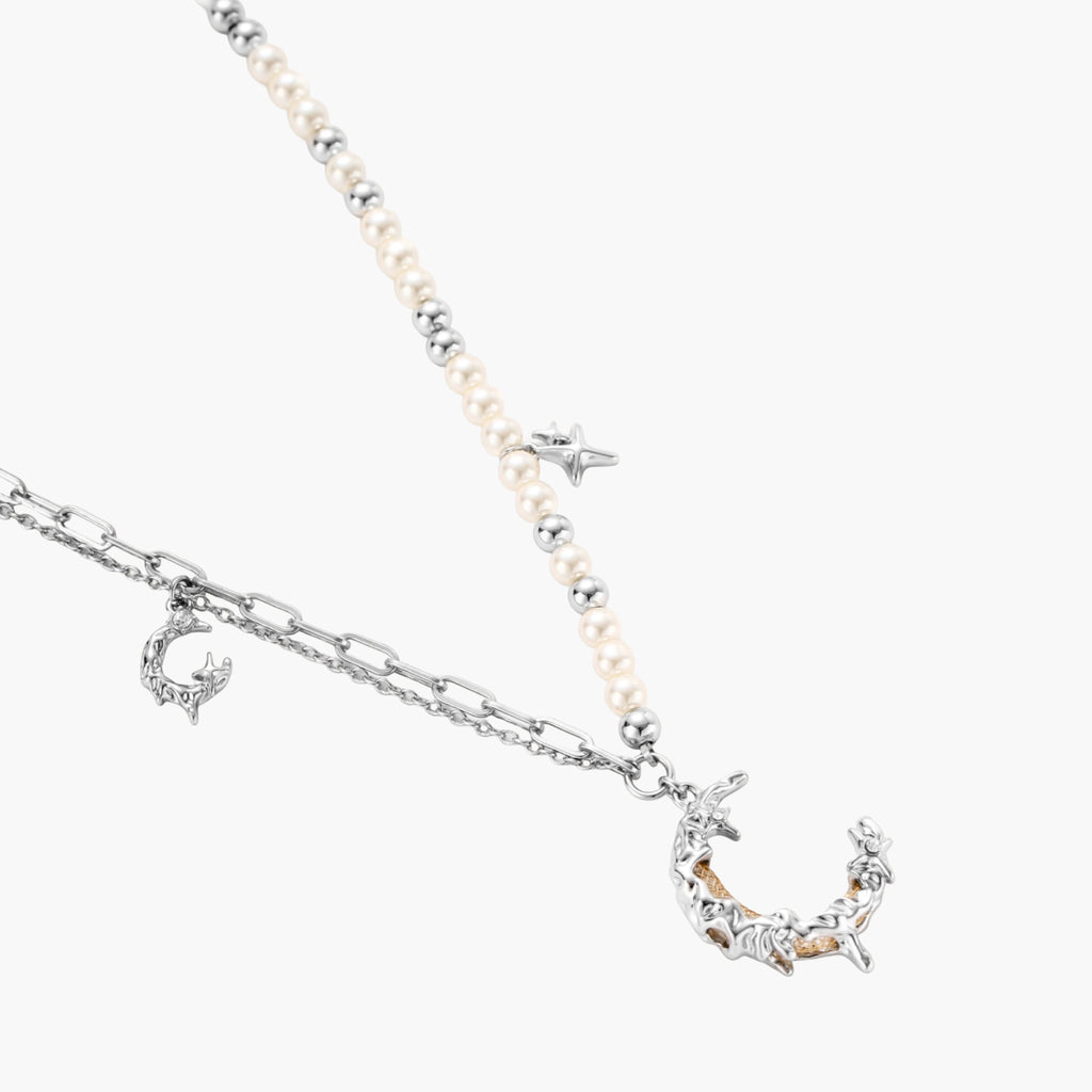 Silver-toned crescent moon pendant with star accents on pearl and chain necklace against white background.