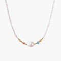 Delicate white beaded necklace with baroque pearl center, gold accents, and coral and aqua gemstones on cream background.