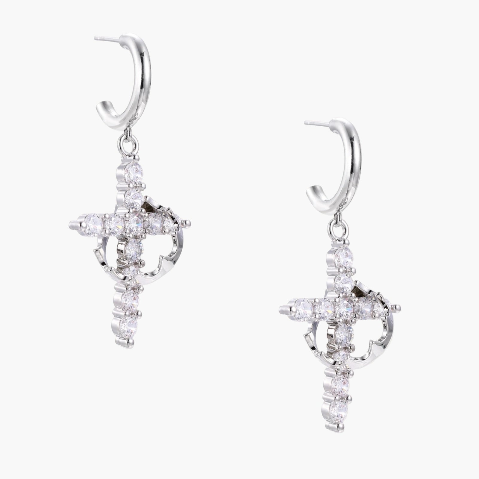 White gold-plated hoop earrings with sparkling zirconia cross charms dangling against cream background