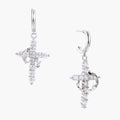 White gold-plated hoop earrings with sparkling zirconia cross charms dangling against cream background