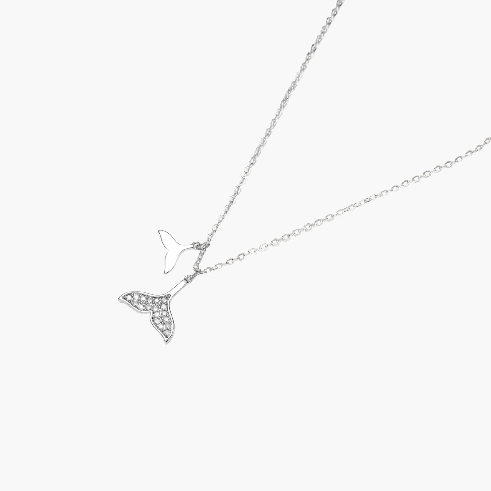 Delicate white gold plated whale tail pendant with pavé crystals on silver chain against cream background.