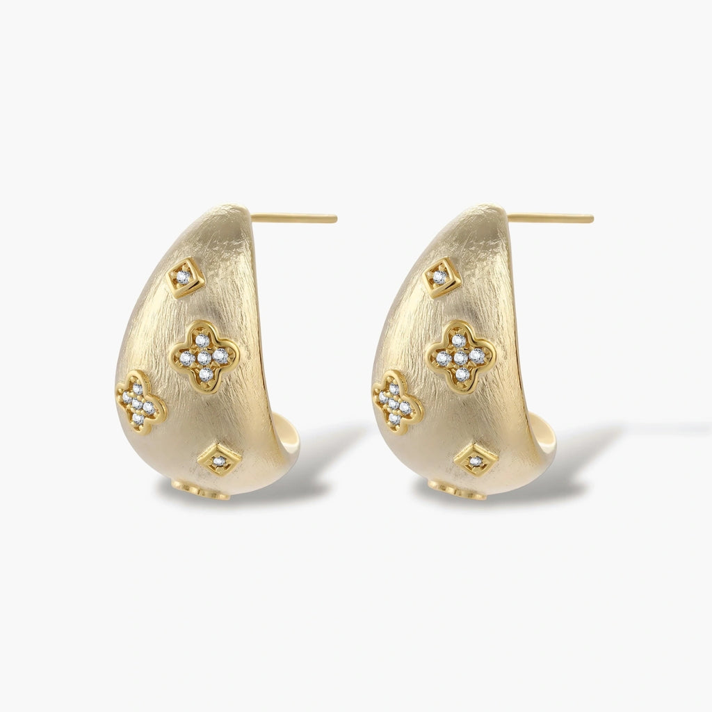Curved gold-plated hoop earrings with four-leaf clover and diamond-shaped crystal details on white background