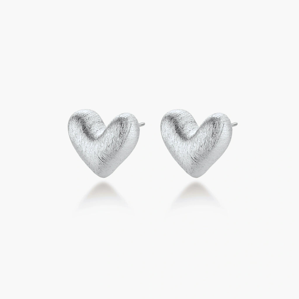 Pair of brushed platinum-plated 925 sterling silver puffy heart stud earrings on a cream background.