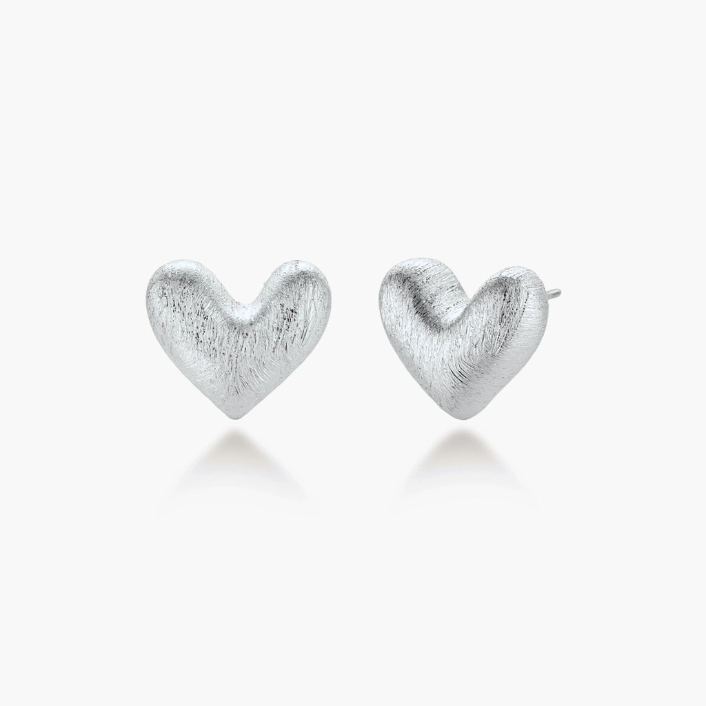 Pair of brushed platinum-plated 925 sterling silver puffy heart stud earrings on a cream background.