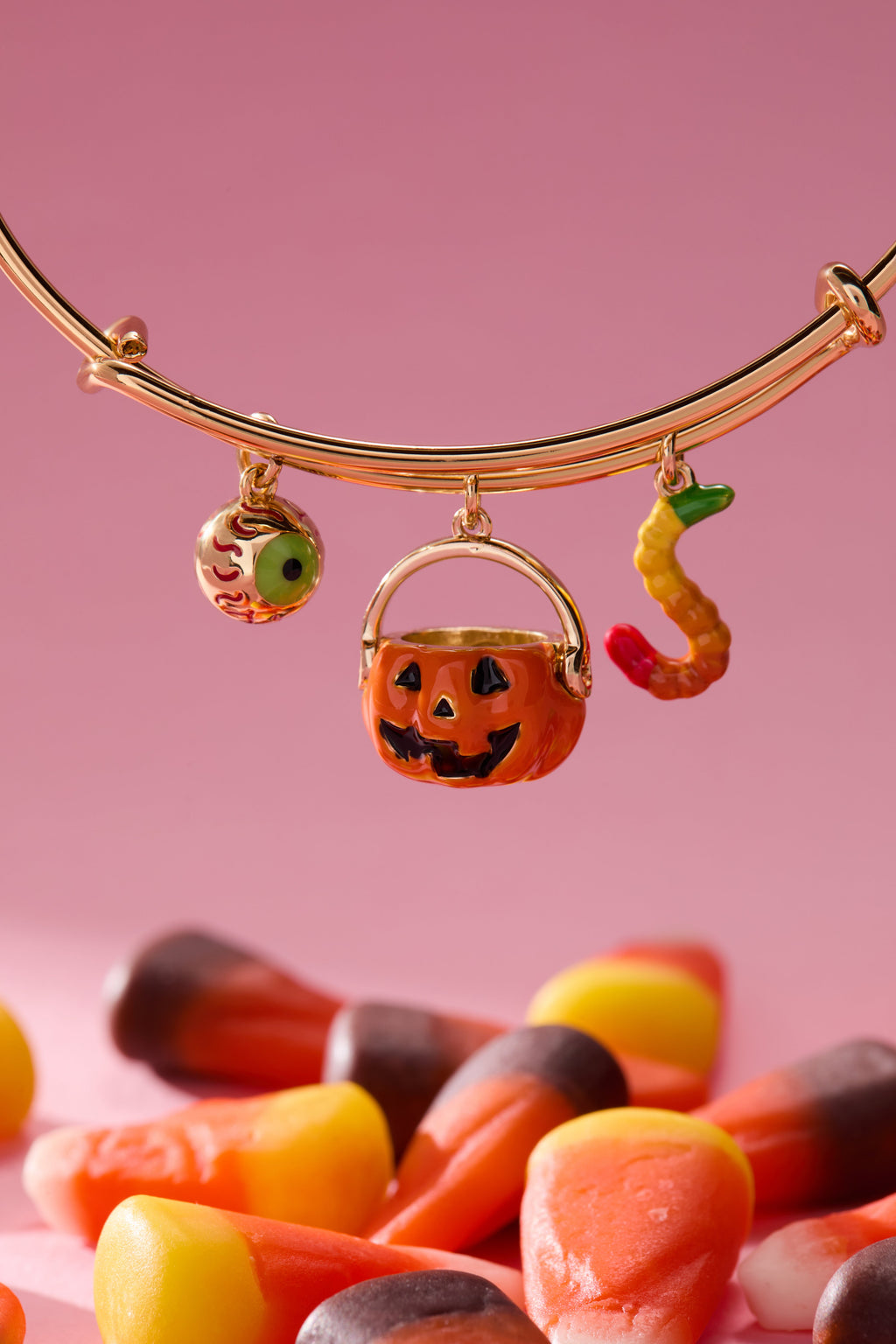 Gold bracelet with Halloween-themed charms on a pink background with candy corn.