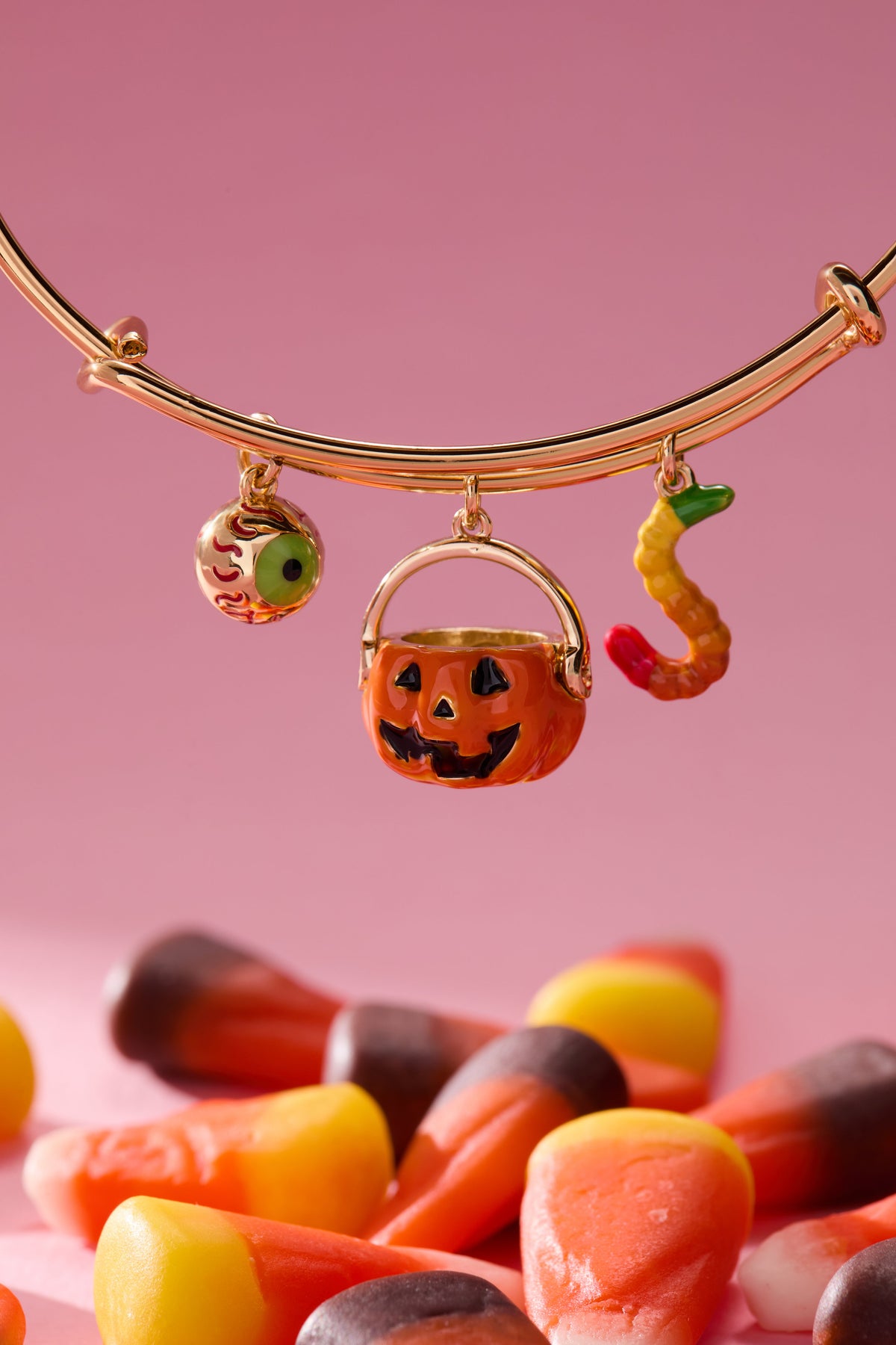 Gold bracelet with Halloween-themed charms on a pink background with candy corn.