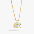 A gold chain necklace with a circular pendant featuring a light green enamel center, a gold hummingbird charm with a clear crystal, and small pale pink floral accents, shown on a light gray background.